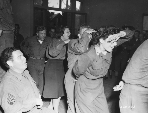 Wacs and nurses form a conga line with combat troops at a rest center in France.